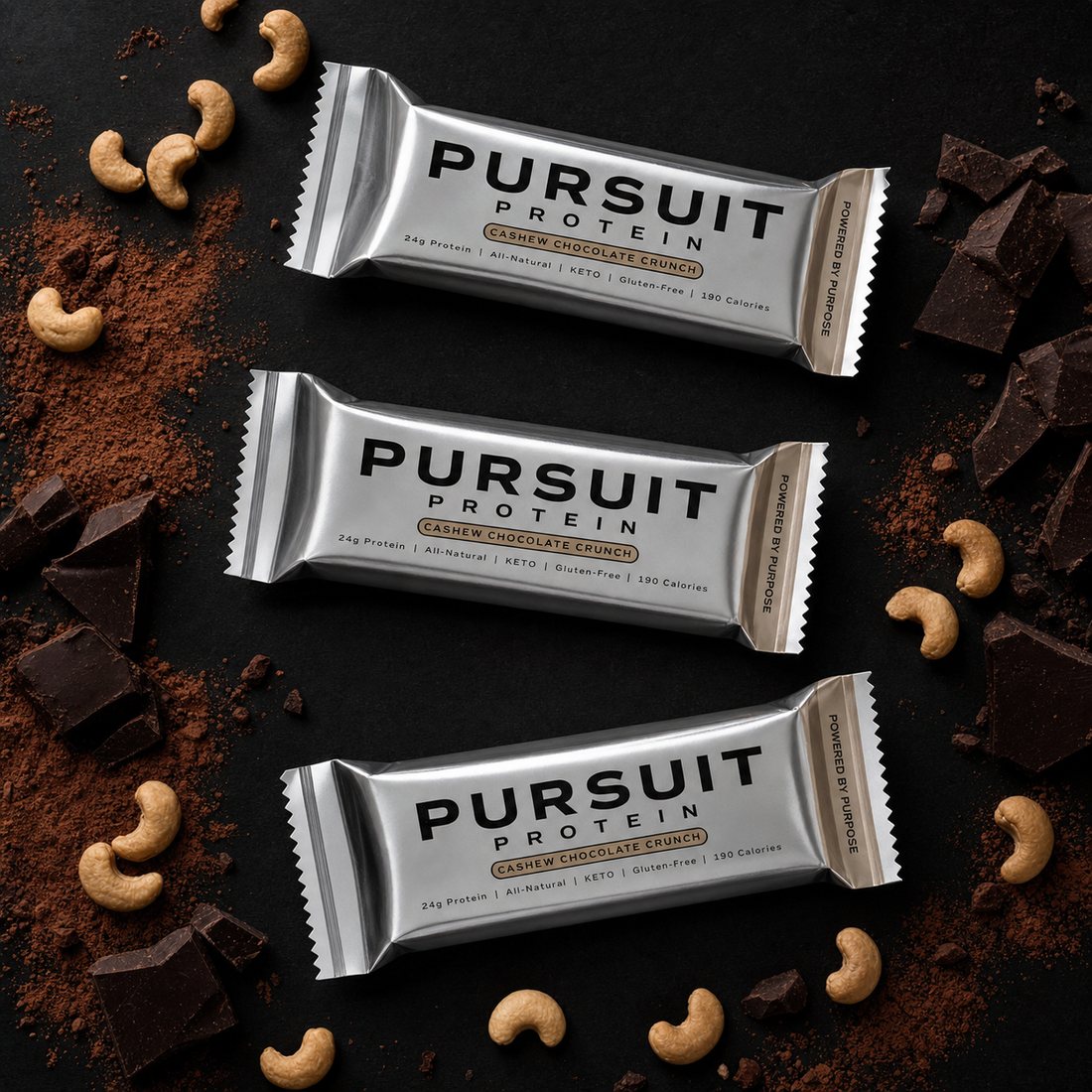 Three Pursuit Protein bars on dark surface with cashews and chocolate